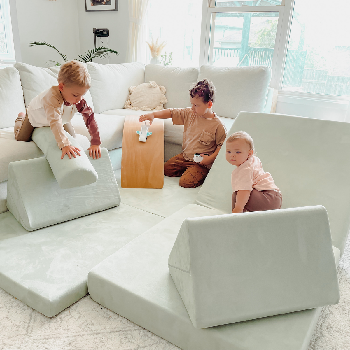 Three kids playing on a modular play couch, featuring soft foam cushions and floor couch pieces designed for kids; a durable and fun Canadian play couch ideal for active toddlers.