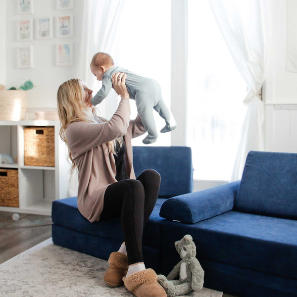 Mom sitting on a modular foam play couch while holding her baby—soft, durable floor couch for kids made with high-quality Canadian materials.